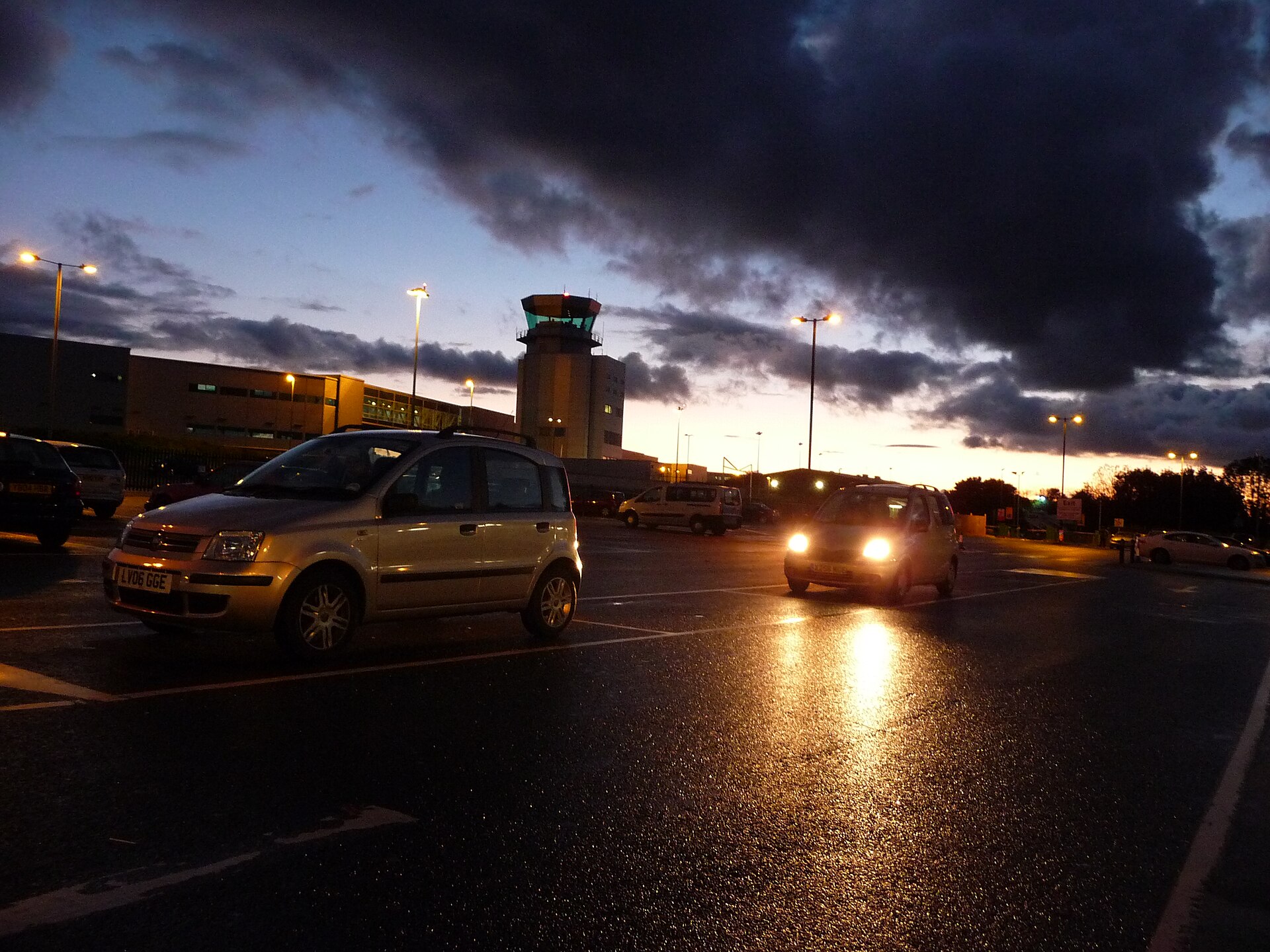 Cars at Bristol Airport's drop-off point at dusk, with the control tower behind.