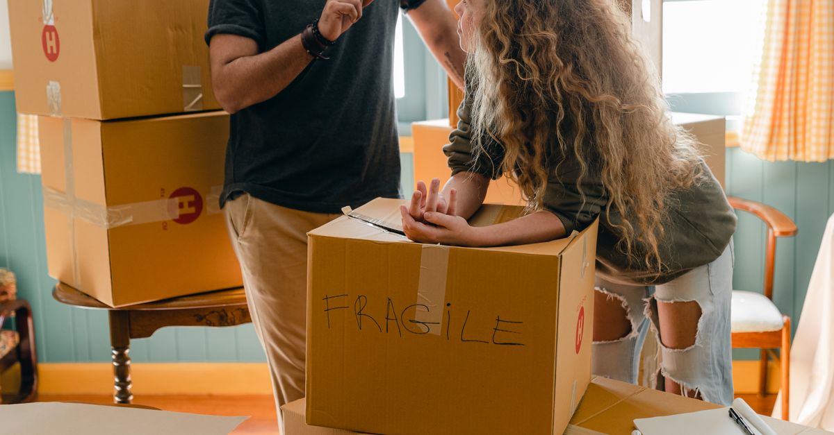A young couple unpacking a cardboard box marked fragile in a shared house