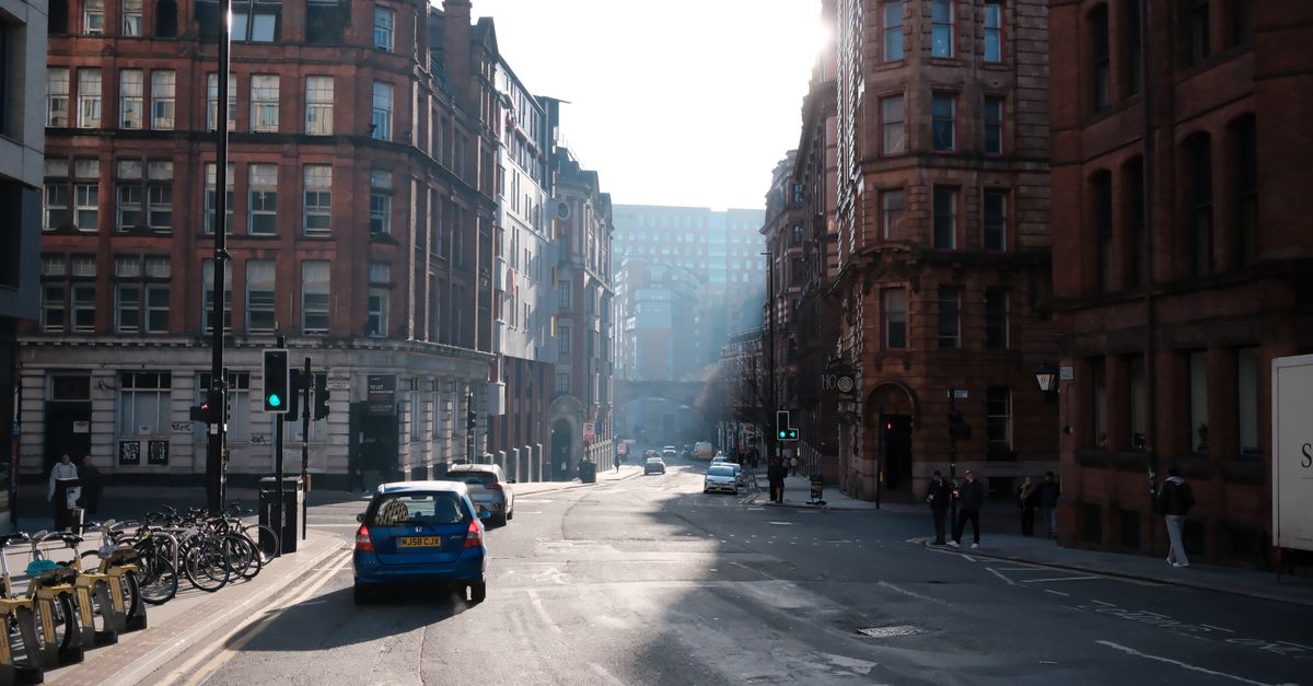 A UK city centre street with traffic and Victorian buildings, hazy in the morning light.