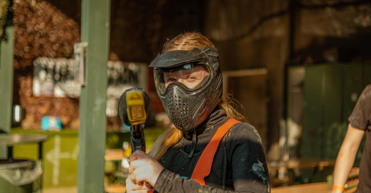 A paintball player in a full-face mask holding a marker outdoors