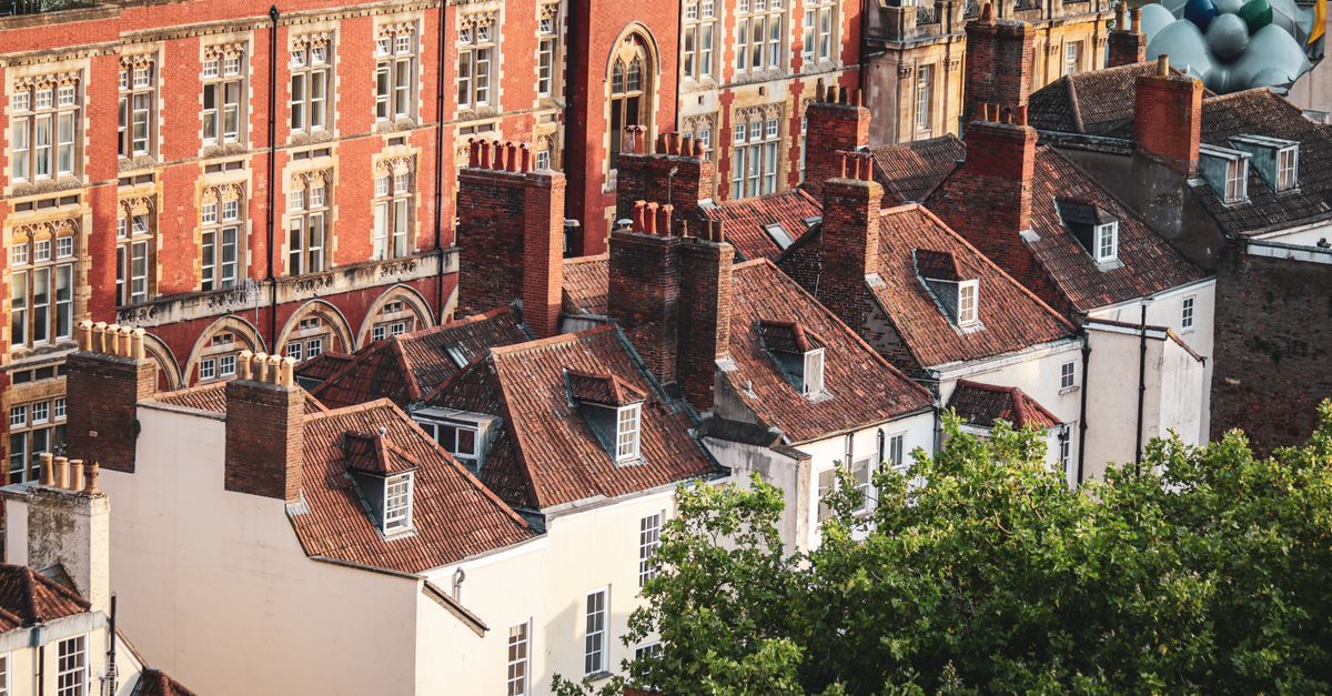 Ornate red-brick university building and rows of Bristol terraced rooftops with chimney stacks, seen from above