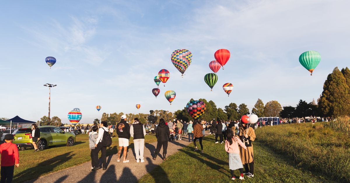 Colourful hot air balloons rising above a crowd at an outdoor festival