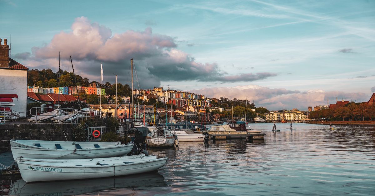 Small boats moored on the harbour with colourful hillside houses behind, one boat marked Sea Cadets