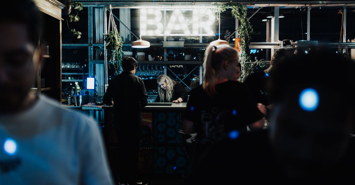 People at a bar lit by a neon 'BAR' sign at night
